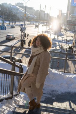 Koyu kıvırcık saçlı, kürk manto, fular, kış soğuğu, şehirde güneşli bir gün..