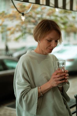 Açık terasta yağmurda genç bir kadın büyük bir bardaktan çay içiyor.