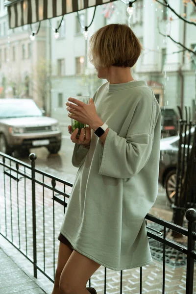 一位年轻女子在露台上的雨中喝着一大杯茶 — 图库照片