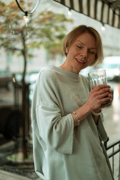 オープンテラスで雨の中の若い女性が大きなガラスからお茶を飲む — ストック写真