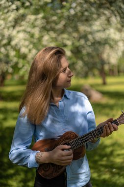 Çiçekli elma bahçesinde ukulele çalan genç ve güzel bir kadın..