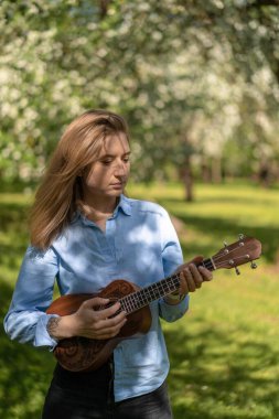 Çiçekli elma bahçesinde ukulele çalan genç ve güzel bir kadın..