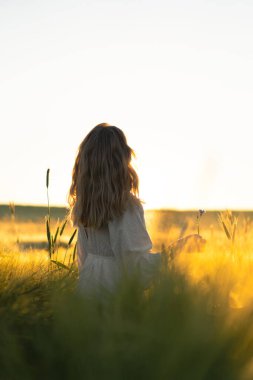 Sabahın erken saatlerinde, buğday tarlasında beyaz elbiseli, uzun sarı saçlı genç ve güzel bir kadın. Yaz, hayalperestlerin, uçan saçların, güneşin altında tarlada koşan bir kadının zamanıdır. seyahat
