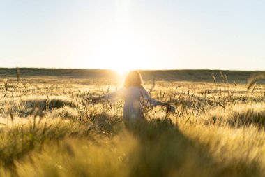 Sabahın erken saatlerinde, buğday tarlasında beyaz elbiseli, uzun sarı saçlı genç ve güzel bir kadın. Yaz, hayalperestlerin, uçan saçların, güneşin altında tarlada koşan bir kadının zamanıdır. seyahat