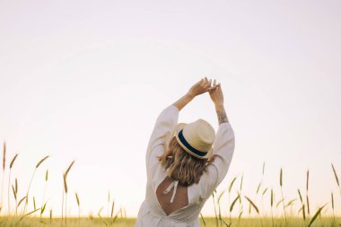 young beautiful woman with blond long hair in a white dress in a straw hat on a wheat field. Flying hair in the sun, summer. Time for dreamers, golden sunset. clipart