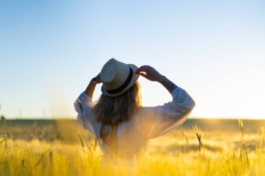 Sabahın erken saatlerinde, buğday tarlasında beyaz elbiseli, uzun sarı saçlı genç ve güzel bir kadın. Yaz, hayalperestlerin, uçan saçların, güneşin altında tarlada koşan bir kadının zamanıdır. seyahat