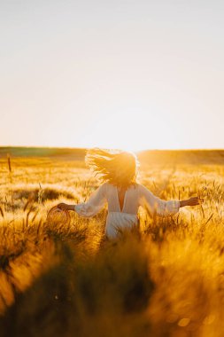 Sabahın erken saatlerinde, buğday tarlasında beyaz elbiseli, uzun sarı saçlı genç ve güzel bir kadın. Yaz, hayalperestlerin, uçan saçların, güneşin altında tarlada koşan bir kadının zamanıdır. seyahat