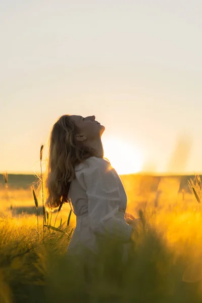 日出时分 一位年轻美丽的女子在麦田里穿着一件白色长裙 一头金发 夏天是梦想家 飘扬的头发 一个女人在阳光下穿过田野的时候 — 图库照片