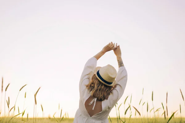 年轻美丽的女人 金发碧眼 穿着白衣 头戴草帽 站在麦田里 在阳光下飘扬的头发 梦想家的时间 金色的日落 — 图库照片