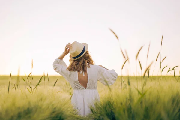 年轻美丽的女人 金发碧眼 穿着白衣 头戴草帽 站在麦田里 在阳光下飘扬的头发 梦想家的时间 金色的日落 — 图库照片