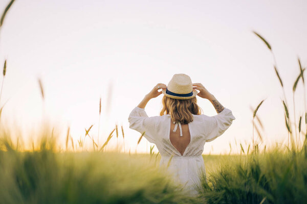 young beautiful woman with blond long hair in a white dress in a straw hat on a wheat field. Flying hair in the sun, summer. Time for dreamers, golden sunset.