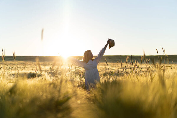 young beautiful woman with long blond hair in a white dress on a wheat field in the early morning at sunrise. Summer is the time for dreamers, flying hair, a woman running across the field in the rays of the sun. travels