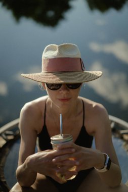 Hasır şapkalı ve trambolinde mayosu olan orta yaşlı güzel bir kadın.