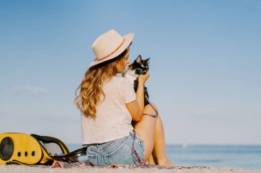 Deniz kıyısında sırt çantasında kedisi olan genç bir kadın. Bir evcil hayvanla seyahat konsepti.