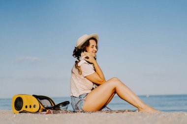 Deniz kıyısında sırt çantasında kedisi olan genç bir kadın. Bir evcil hayvanla seyahat konsepti.