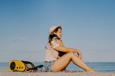 Deniz kıyısında sırt çantasında kedisi olan genç bir kadın. Bir evcil hayvanla seyahat konsepti.