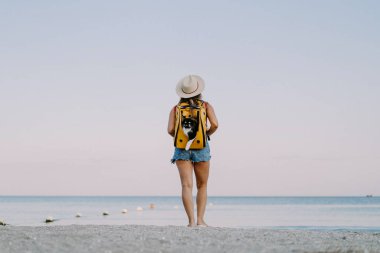 Deniz kıyısında sırt çantasında kedisi olan genç bir kadın. Bir evcil hayvanla seyahat konsepti.