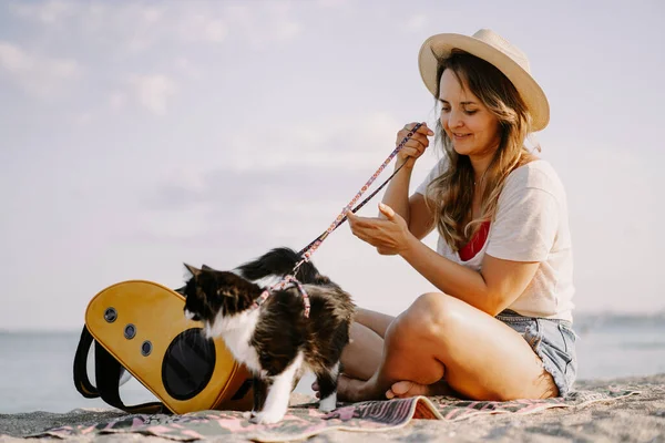 young woman with a cat in a backpack on the seashore. Travel concept with a pet.