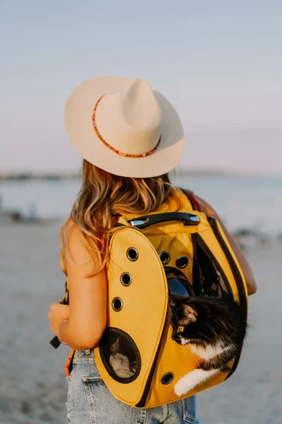 young woman with a cat in a backpack on the seashore. Travel concept with a pet.