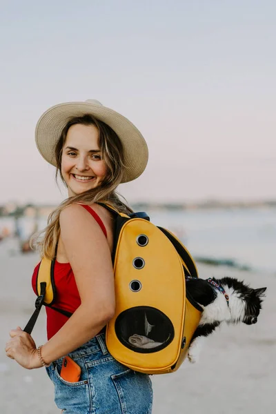 young woman with a cat in a backpack on the seashore. Travel concept with a pet.