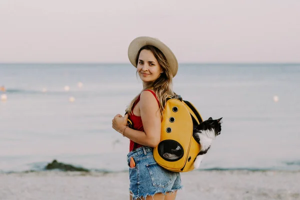 young woman with a cat in a backpack on the seashore. Travel concept with a pet.