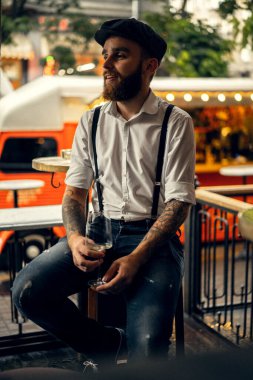 Caddedeki kafede elinde bir bardak şarapla sakallı genç bir adam. Şehirde beyaz gömlekli ve pantolon askısı takan romantik bir adam. Peaky Blinders. eski fasyon retro.