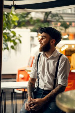 Caddedeki kafede elinde bir bardak şarapla sakallı genç bir adam. Şehirde beyaz gömlekli ve pantolon askısı takan romantik bir adam. Peaky Blinders. eski fasyon retro.