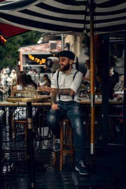 Caddedeki kafede elinde bir bardak şarapla sakallı genç bir adam. Şehirde beyaz gömlekli ve pantolon askısı takan romantik bir adam. Peaky Blinders. eski fasyon retro.