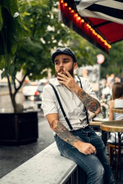 Caddedeki bir kafede sigara içen sakallı genç bir adam. Şehirde beyaz gömlekli ve pantolon askısı takan romantik bir adam. Peaky Blinders. eski moda retro.