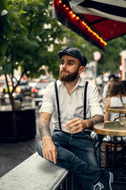 Caddedeki bir kafede sigara içen sakallı genç bir adam. Şehirde beyaz gömlekli ve pantolon askısı takan romantik bir adam. Peaky Blinders. eski moda retro.