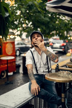 Caddedeki bir kafede sigara içen sakallı genç bir adam. Şehirde beyaz gömlekli ve pantolon askısı takan romantik bir adam. Peaky Blinders. eski moda retro.