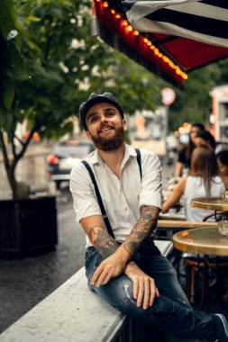 Caddedeki bir kafede sigara içen sakallı genç bir adam. Şehirde beyaz gömlekli ve pantolon askısı takan romantik bir adam. Peaky Blinders. eski moda retro.