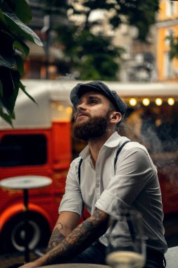 Caddedeki bir kafede sigara içen sakallı genç bir adam. Şehirde beyaz gömlekli ve pantolon askısı takan romantik bir adam. Peaky Blinders. eski moda retro.