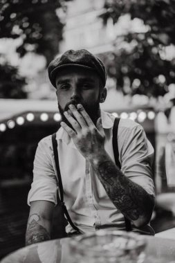 Caddedeki bir kafede sigara içen sakallı genç bir adam. Şehirde beyaz gömlekli ve pantolon askısı takan romantik bir adam. Peaky Blinders. eski moda retro.