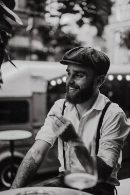Caddedeki bir kafede sigara içen sakallı genç bir adam. Şehirde beyaz gömlekli ve pantolon askısı takan romantik bir adam. Peaky Blinders. eski moda retro.