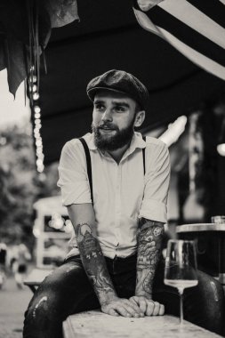 Caddedeki kafede elinde bir bardak şarapla sakallı genç bir adam. Şehirde beyaz gömlekli ve pantolon askısı takan romantik bir adam. Peaky Blinders. eski fasyon retro.