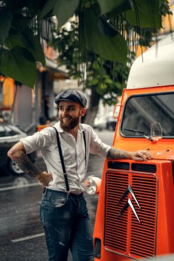 Caddedeki kafede elinde bir bardak şarapla sakallı genç bir adam. Şehirde beyaz gömlekli ve pantolon askısı takan romantik bir adam. Peaky Blinders. eski fasyon retro.