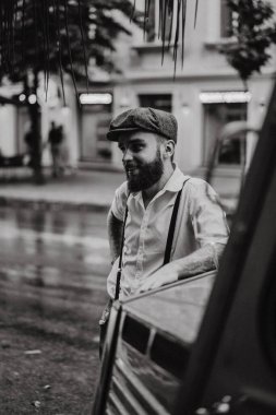 Caddedeki bir kafede sigara içen sakallı genç bir dövmeli adam. Şehirde beyaz gömlekli ve pantolon askısı takan romantik bir adam. Peaky Blinders. eski moda retro.