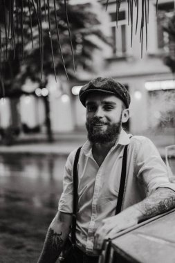 Caddedeki bir kafede sigara içen sakallı genç bir dövmeli adam. Şehirde beyaz gömlekli ve pantolon askısı takan romantik bir adam. Peaky Blinders. eski moda retro.