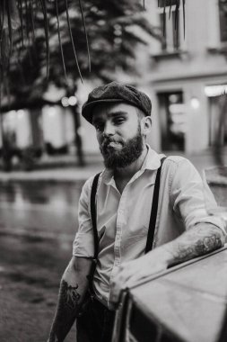 Caddedeki bir kafede sigara içen sakallı genç bir dövmeli adam. Şehirde beyaz gömlekli ve pantolon askısı takan romantik bir adam. Peaky Blinders. eski moda retro.