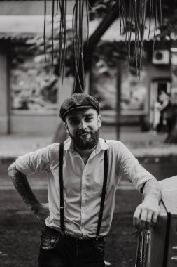 Caddedeki bir kafede sigara içen sakallı genç bir dövmeli adam. Şehirde beyaz gömlekli ve pantolon askısı takan romantik bir adam. Peaky Blinders. eski moda retro.