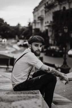 Genç, sakallı, caddedeki bardaktan şarap içen adam. Şehirde beyaz gömlekli, şapkalı ve pantolon askısı takan romantik bir adam. Peaky Blinders. Eski moda, eski moda..