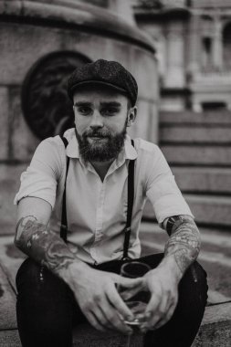 Genç, sakallı, caddedeki bardaktan şarap içen adam. Şehirde beyaz gömlekli, şapkalı ve pantolon askısı takan romantik bir adam. Peaky Blinders. Eski moda, eski moda..