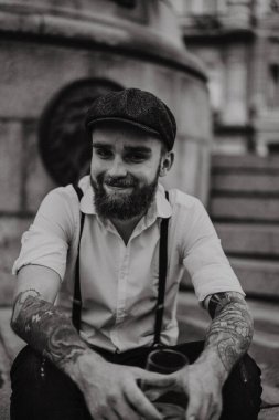 Genç, sakallı, caddedeki bardaktan şarap içen adam. Şehirde beyaz gömlekli, şapkalı ve pantolon askısı takan romantik bir adam. Peaky Blinders. Eski moda, eski moda..