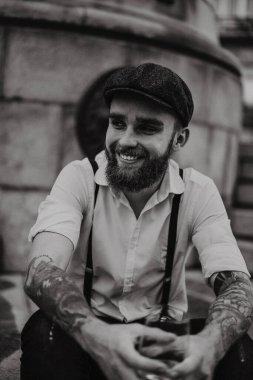 Genç, sakallı, caddedeki bardaktan şarap içen adam. Şehirde beyaz gömlekli, şapkalı ve pantolon askısı takan romantik bir adam. Peaky Blinders. Eski moda, eski moda..