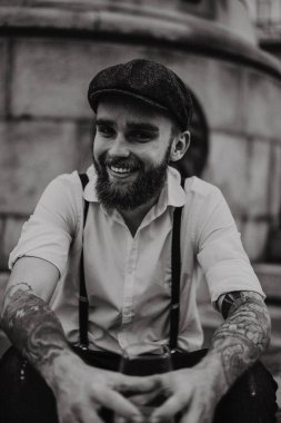 Genç, sakallı, caddedeki bardaktan şarap içen adam. Şehirde beyaz gömlekli, şapkalı ve pantolon askısı takan romantik bir adam. Peaky Blinders. Eski moda, eski moda..