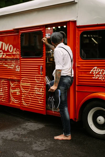 Young bearded tattooed man. A romantic guy in a white shirt, cap and suspenders walks in the city. revolves around a lamppost. Peaky Blinders. old-fashioned, retro.