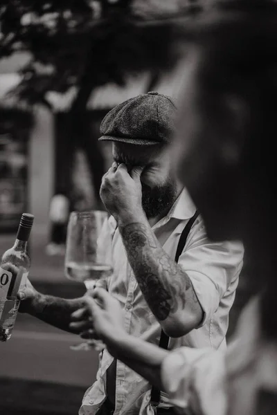 Young bearded tattooed man. A romantic guy in a white shirt, cap and suspenders walks in the city. revolves around a lamppost. Peaky Blinders. old-fashioned, retro.