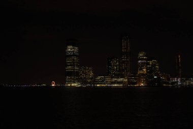 New York Şehri Manhattan, gece vakti Hudson Nehri üzerinde yansımalarla aydınlanan gökdelenlerle..