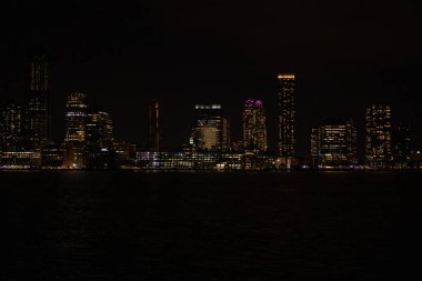 New York Şehri Manhattan, gece vakti Hudson Nehri üzerinde yansımalarla aydınlanan gökdelenlerle..